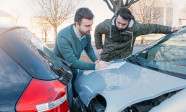 Two men writing a car insurance claim after a car crash