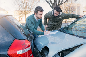 Two men writing a car insurance claim after a car crash